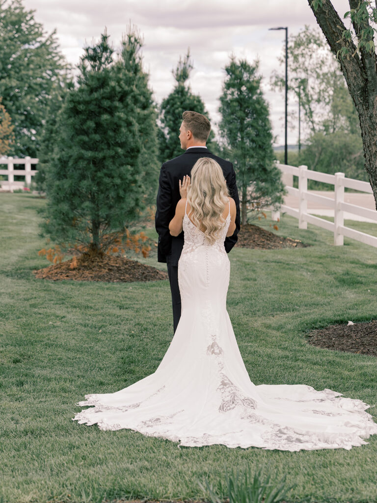 Bride and groom back-to-back first touch among evergreens at Bella Giornata, Byron Center MI