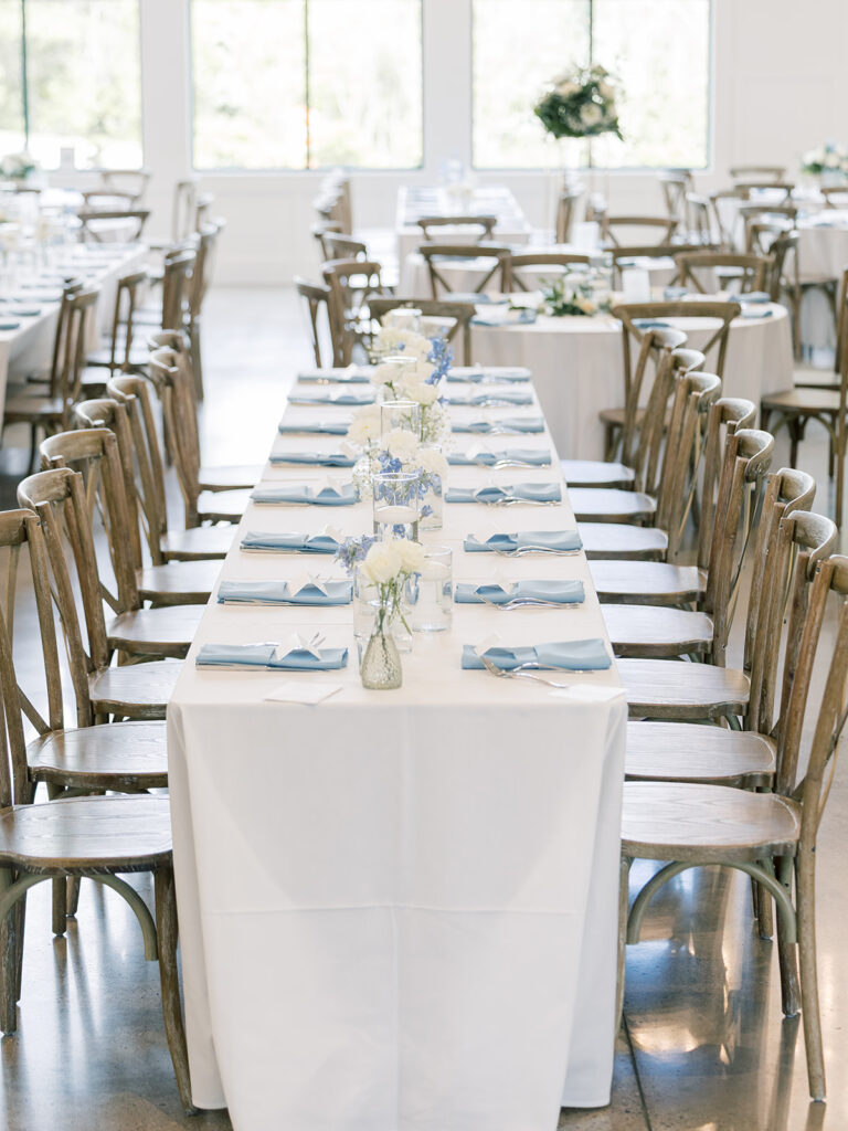 Long reception tables with white linens, dusty blue napkins and crossback chairs at Bella Giornata